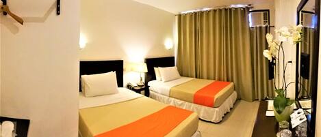 A hotel room with two beds, a nightstand with a lamp, a mirror, a window with curtains, and a vase with flowers.