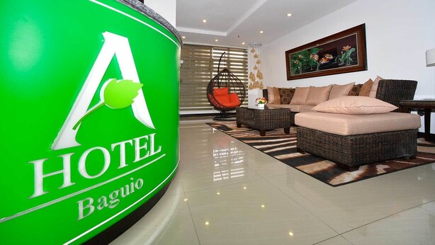 A modern hotel lobby with a large green sign, wicker furniture, and a framed painting on the wall. - A Hotel Baguio (Baguio)