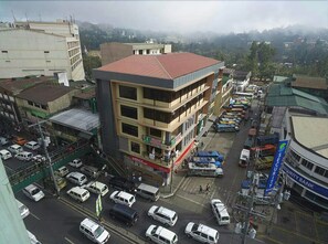 A multi-story building with a red roof, surrounded by parked vehicles and a busy street. - A Hotel Baguio (Baguio)