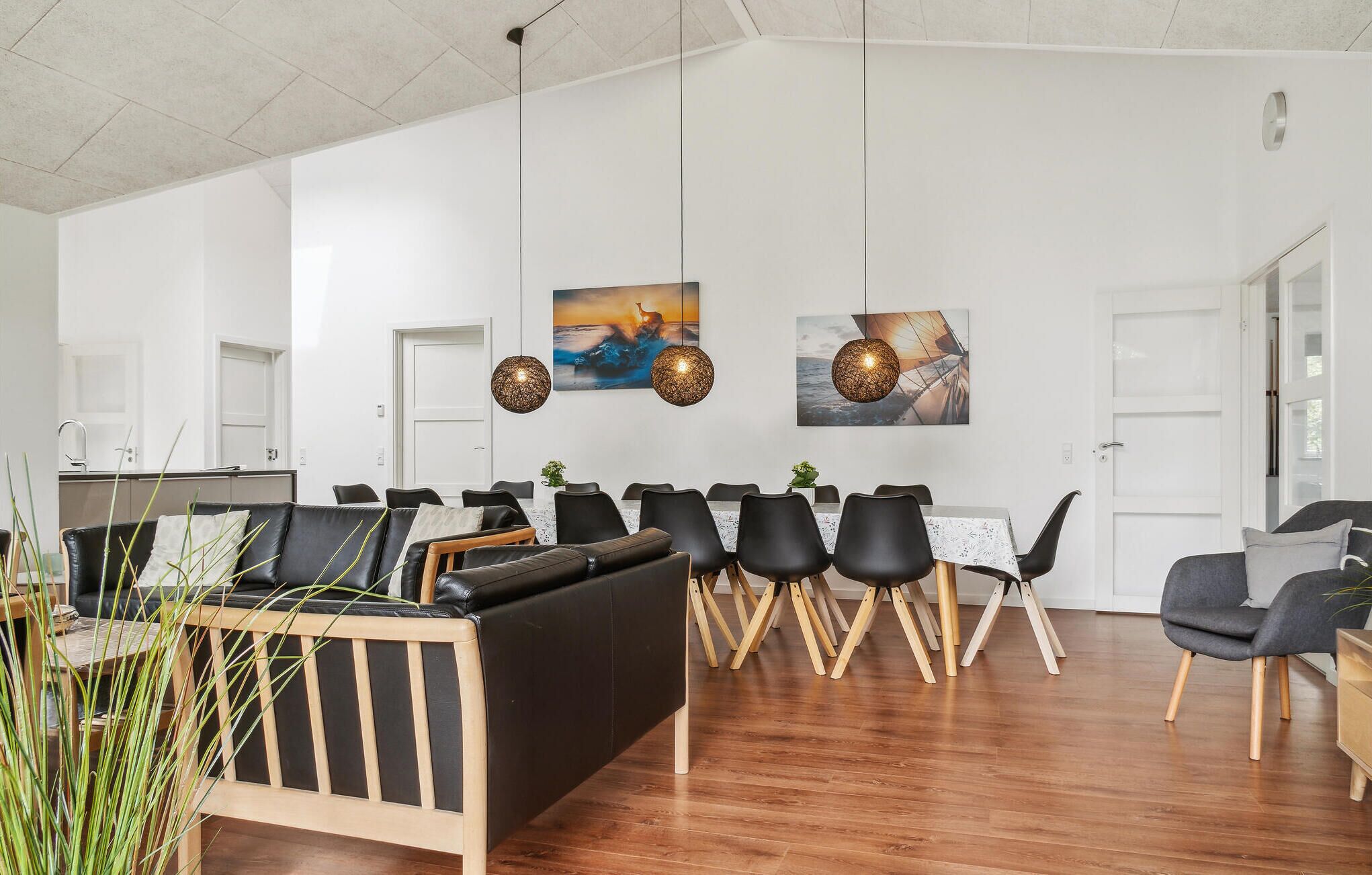 Un espace de vie moderne et ouvert, avec un plancher en bois, des canapés en cuir noir et une table à manger avec des chaises.