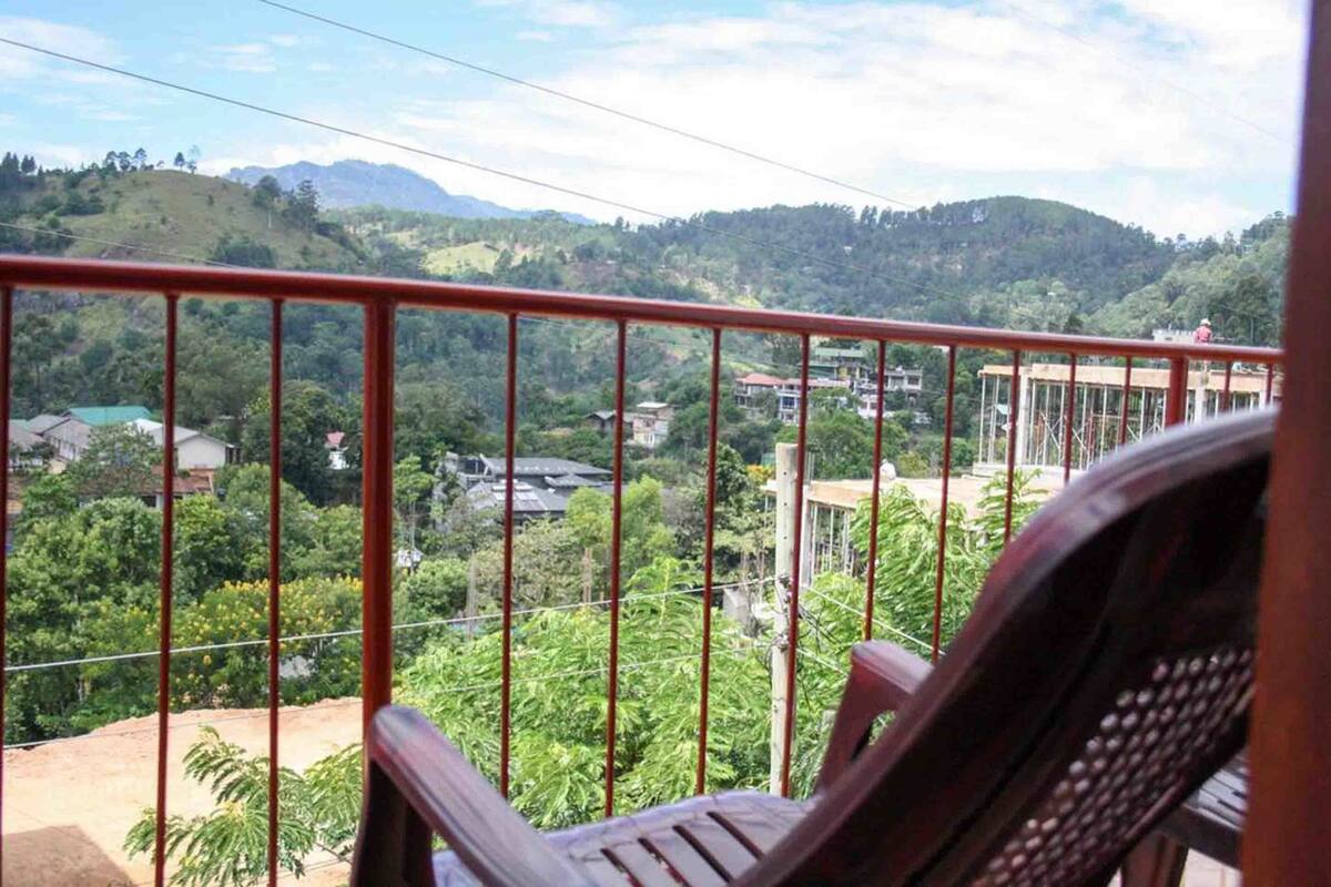 A balcony with a view of a hilly landscape, a chair, and a railing.