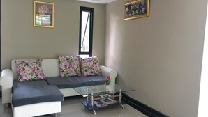 Un salon moderne avec un canapé, deux coussins à motifs floraux, une table basse en verre et deux tableaux encadrés accrochés aux murs.