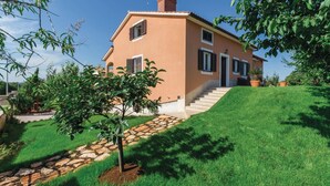Uma casa de dois andares com um caminho de pedra que leva à porta da frente, cercada por grama verde exuberante e árvores.