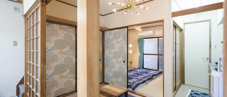 A traditional Japanese-style room with tatami flooring, a shoji screen, a low wooden bed, and a ceiling fan.