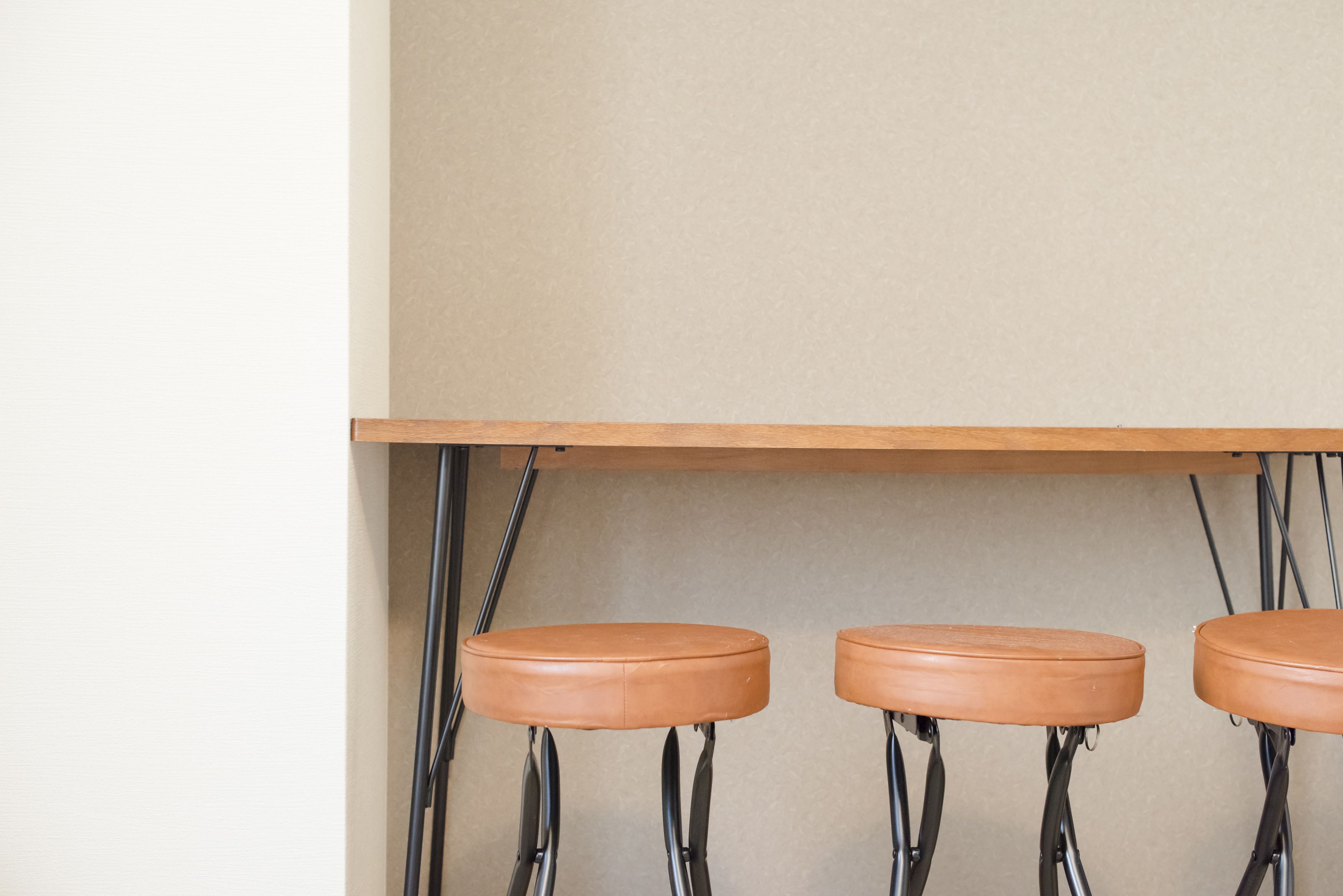 Trois tabourets de bar en bois, dotés de pieds en métal et d’assises en cuir, sont placés sous une étagère en bois, le tout adossé à un mur uni.