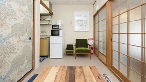Ein traditioneller japanischer Raum mit Tatami-Bodenbelag, einem Shoji-Bildschirm, einem grünen Stuhl, einer kleinen Küchenzeile und einem motivierenden Plakat.