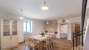 A spacious kitchen with a dining table, white cabinets, and a stone wall. - Beautiful home in Bokordici (Bokordici)
