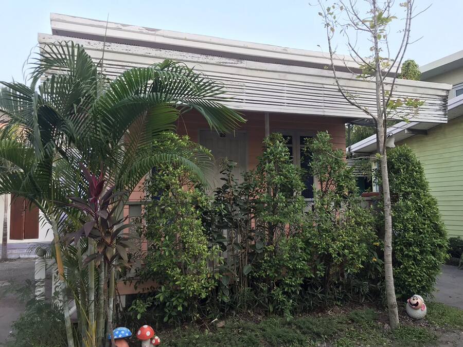Una casa residencial con porche, rodeada de plantas y árboles.