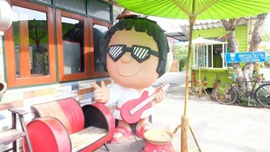 A cartoon character with a guitar outside a building with a green umbrella.