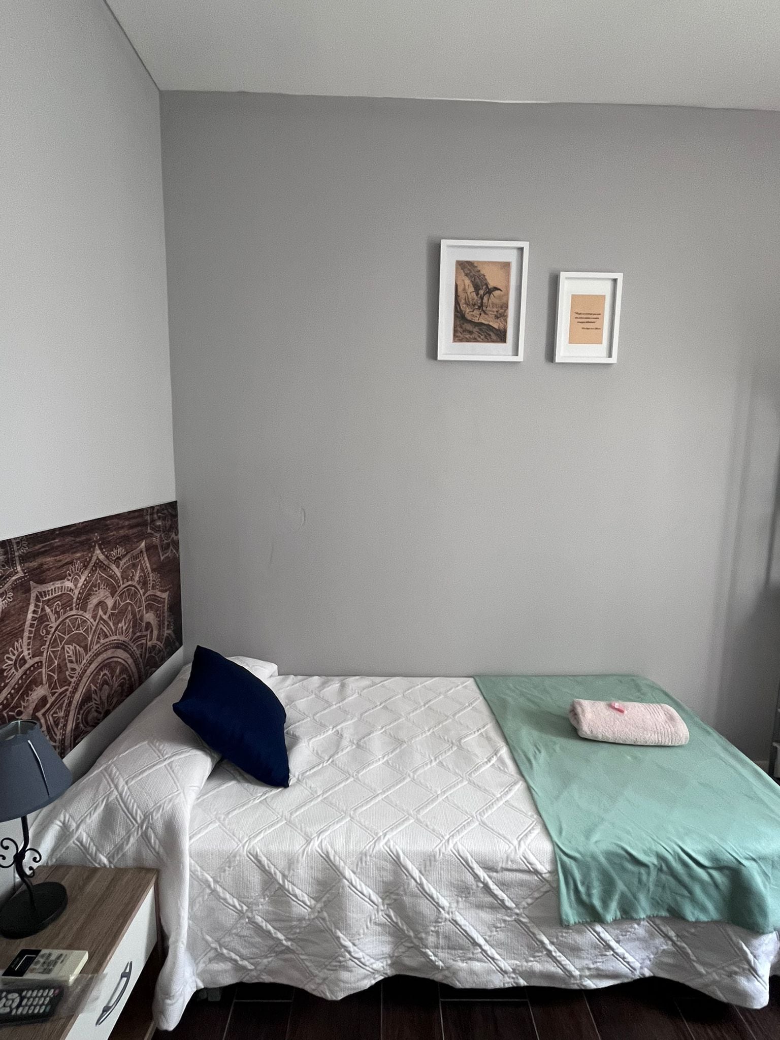 A neatly arranged bedroom with a bed, a bedside table with a lamp, and two framed pictures on the wall.