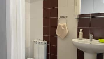 Casa de banho com lavatório branco, suporte de toalhas, radiador e sanita.