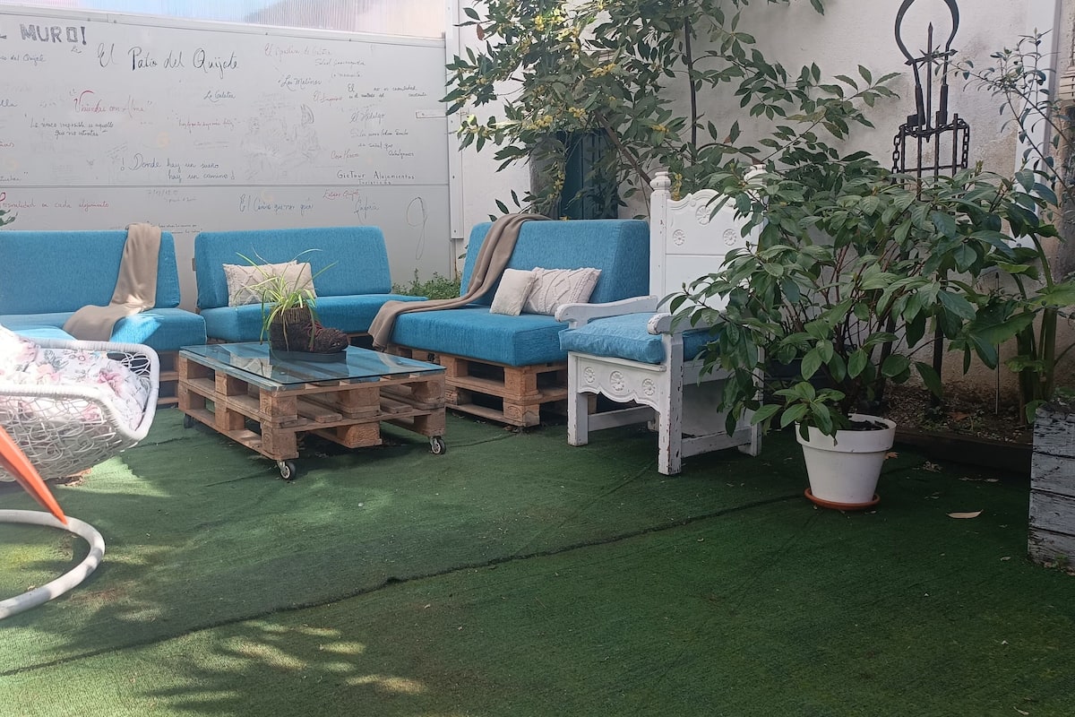 A patio with blue sofas, a glass coffee table, and a white chair. There is a whiteboard with writings and a potted plant.