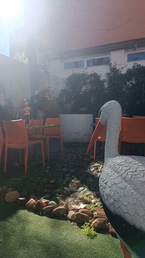 A bird sculpture in an outdoor area with tables and chairs, surrounded by rocks and greenery. - El Sueño del Quijote (Alcala de Henares)