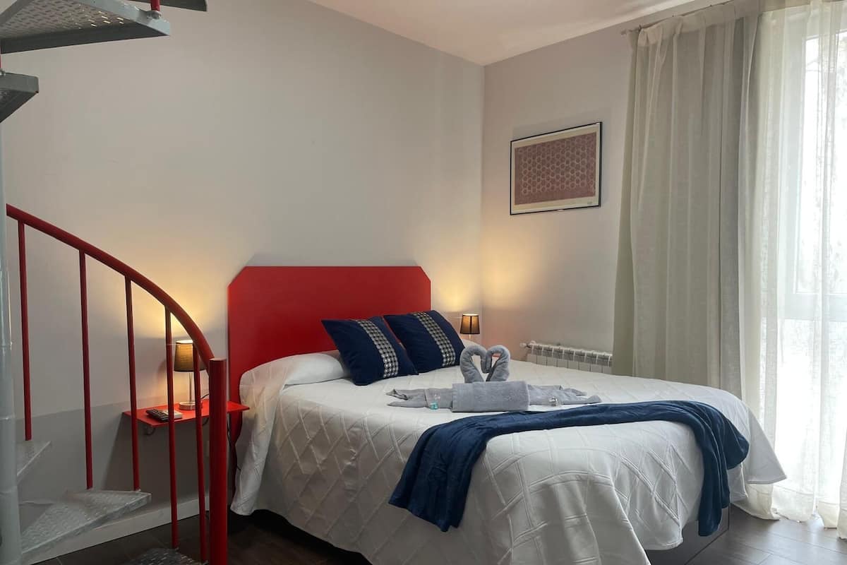 A hotel room with a red headboard, a bed with white bedding, a blue throw blanket, and a towel arrangement on the bed.