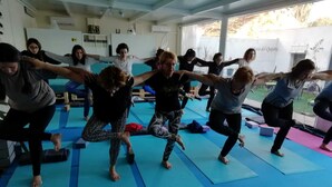 A group of people in a room with blue mats on the floor, engaged in a stretching exercise. - El Sueño del Quijote (Alcala de Henares)