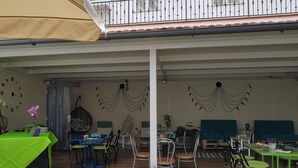 An outdoor dining area with tables and chairs, a covered seating area, and a decorative wall with hanging lights. - El Sueño del Quijote (Alcala de Henares)