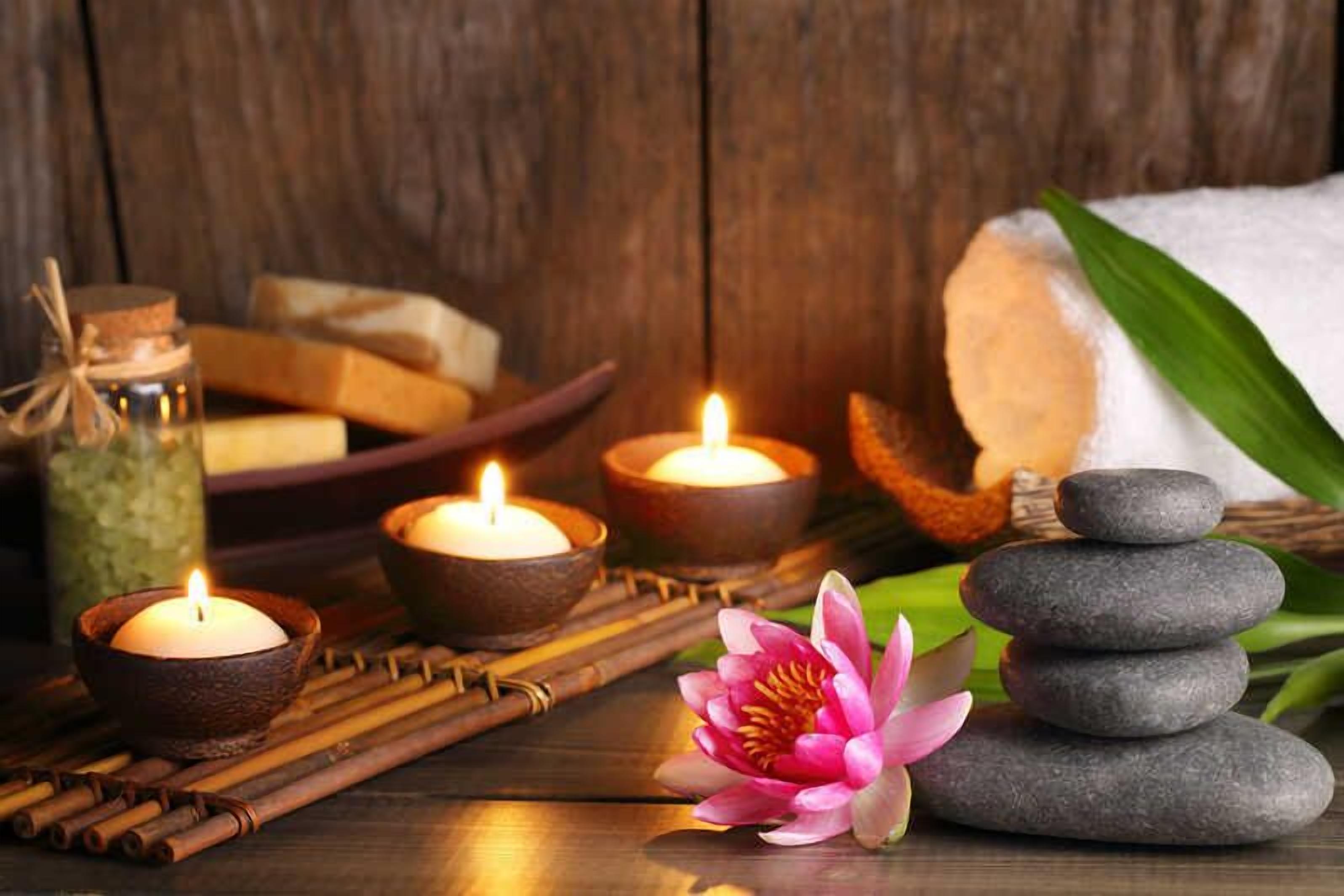 A wooden table with candles, a lotus flower, and a stack of stones.