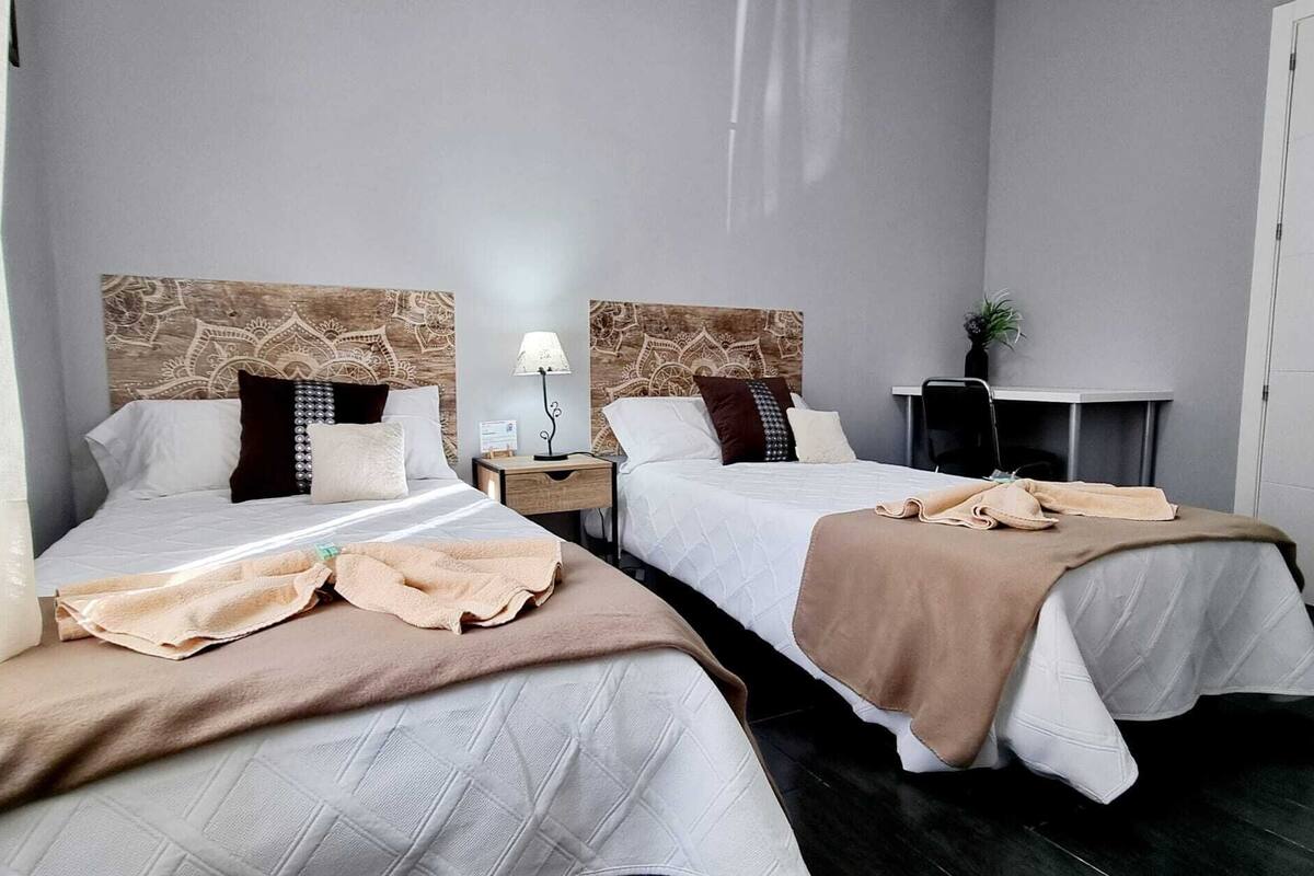 A hotel room with two beds, each with a headboard, bedside tables, and a lamp.