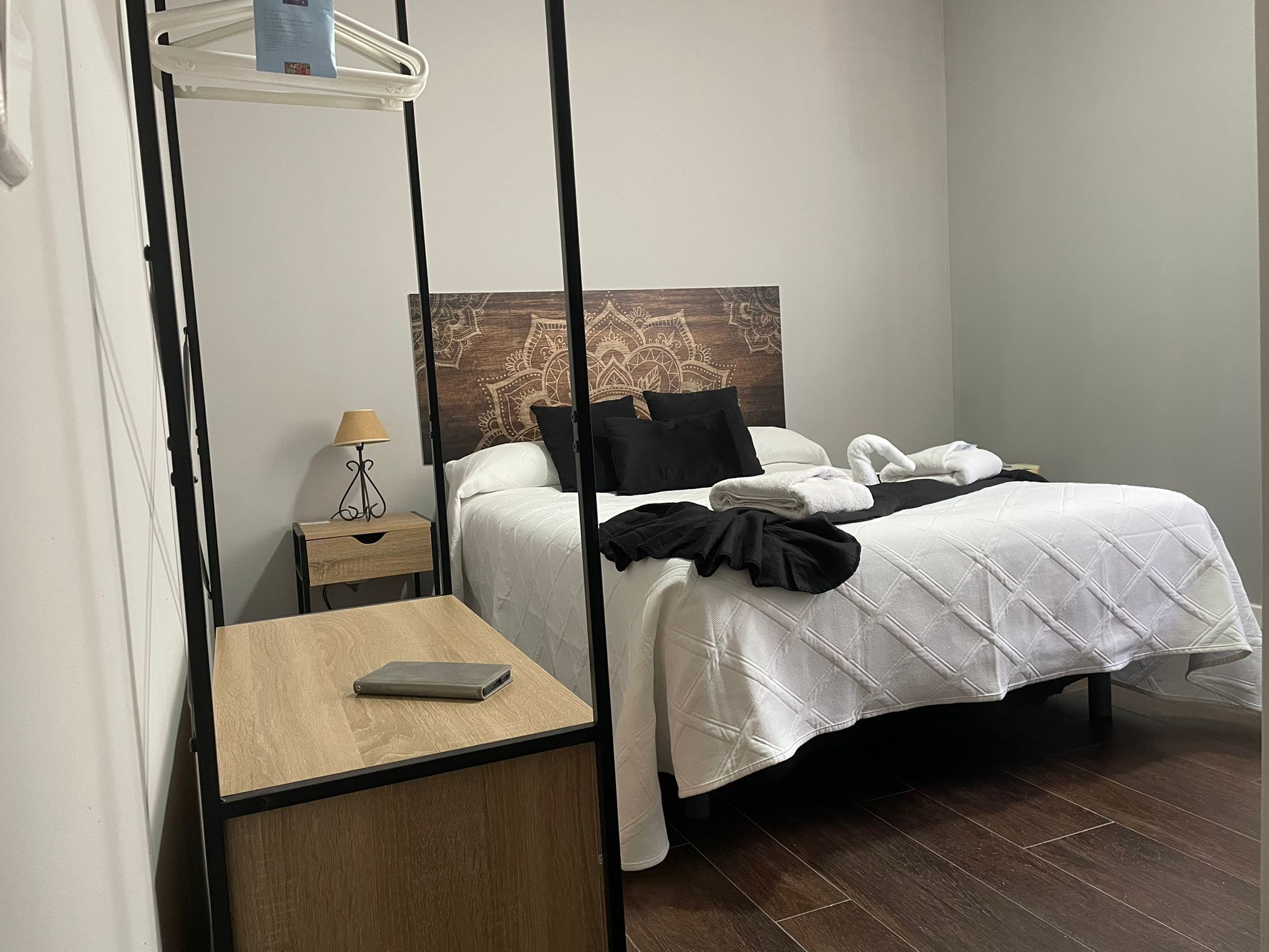 Habitación de hotel con cama, mesita de noche con lámpara, una pequeña mesa de madera y aire acondicionado instalado en la pared.