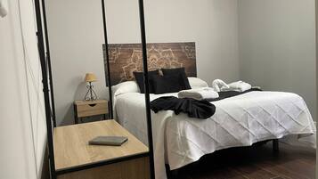 Habitación de hotel con cama, mesita de noche con lámpara, una pequeña mesa de madera y aire acondicionado instalado en la pared.