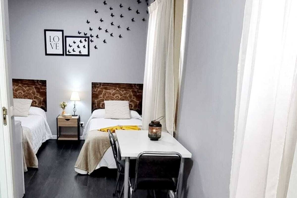 A hotel room with two beds, a dining table, and a small table with a lamp.