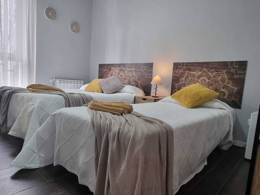 Habitación de hotel con dos camas, una silla, una mesita de noche con lámpara y un radiador.