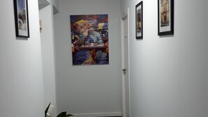 A hallway with white walls, a large abstract painting, and framed pictures. - El Sueño del Quijote (Alcala de Henares)
