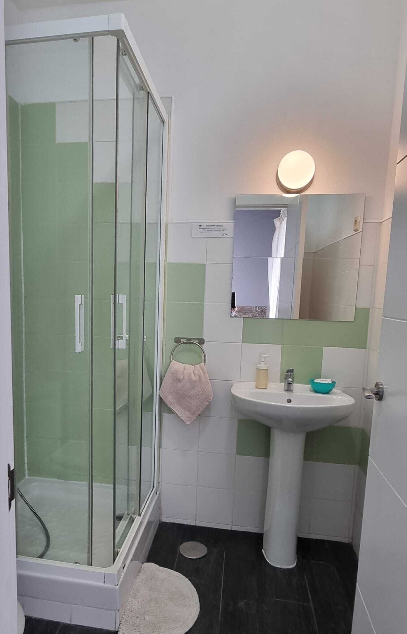 Un baño con cabina de ducha de vidrio, lavamanos pedestal, espejo y toallero.