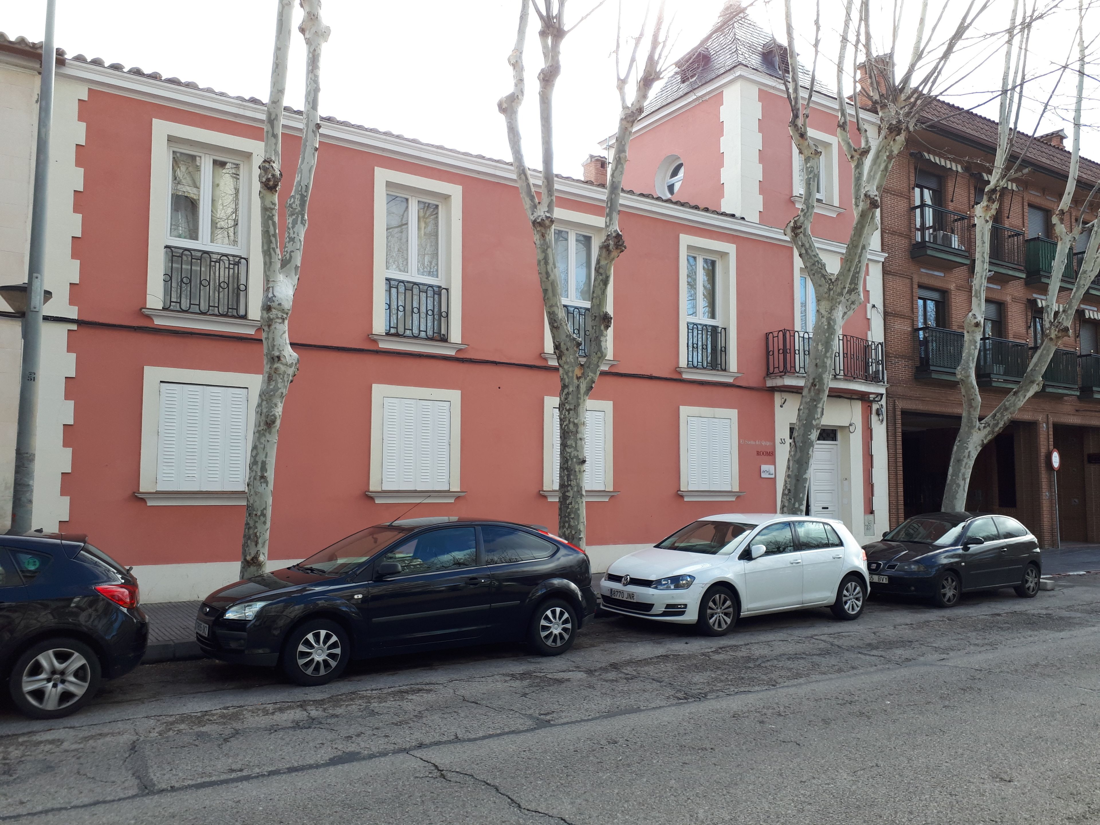A row of parked cars in front of a building with multiple windows and balconies.