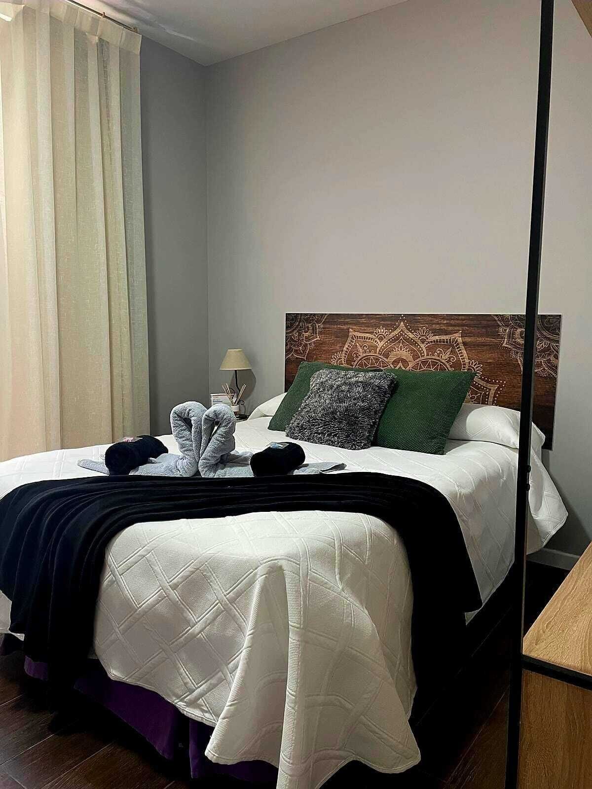 Een net opgemaakt bed met een wit gebordureerd dekbedovertrek, een donker hoofdbord en decoratieve kussens.