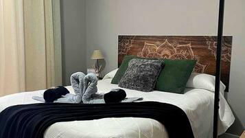Een net opgemaakt bed met een wit gebordureerd dekbedovertrek, een donker hoofdbord en decoratieve kussens.