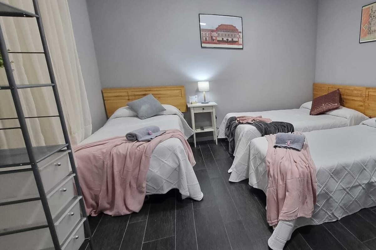A hotel room with three beds, a small desk, a chair, and a ladder.