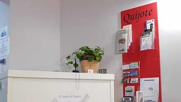 Un mostrador de recepción con un logotipo, una planta en maceta y un tablón de anuncios con varios elementos.