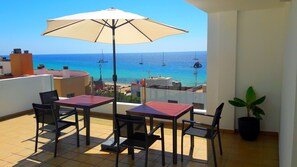 A balcony with two tables and chairs, a large umbrella, and a potted plant.
