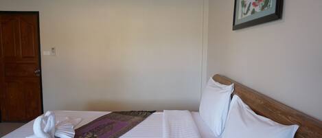 A hotel room with a bed, a wooden headboard, a wall-mounted air conditioner, a framed picture, and a door.