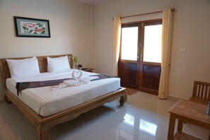 Una cama bien hecha con sábanas blancas y un arreglo decorativo de almohadas con forma de cisne. Tiene un cabecero de madera, una mesita de noche con una lámpara y una ventana con cortinas.