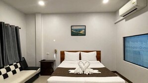 Una habitación de hotel moderna con una cama grande, una mesita de noche pequeña, un aire acondicionado de pared y un ventanal amplio.
