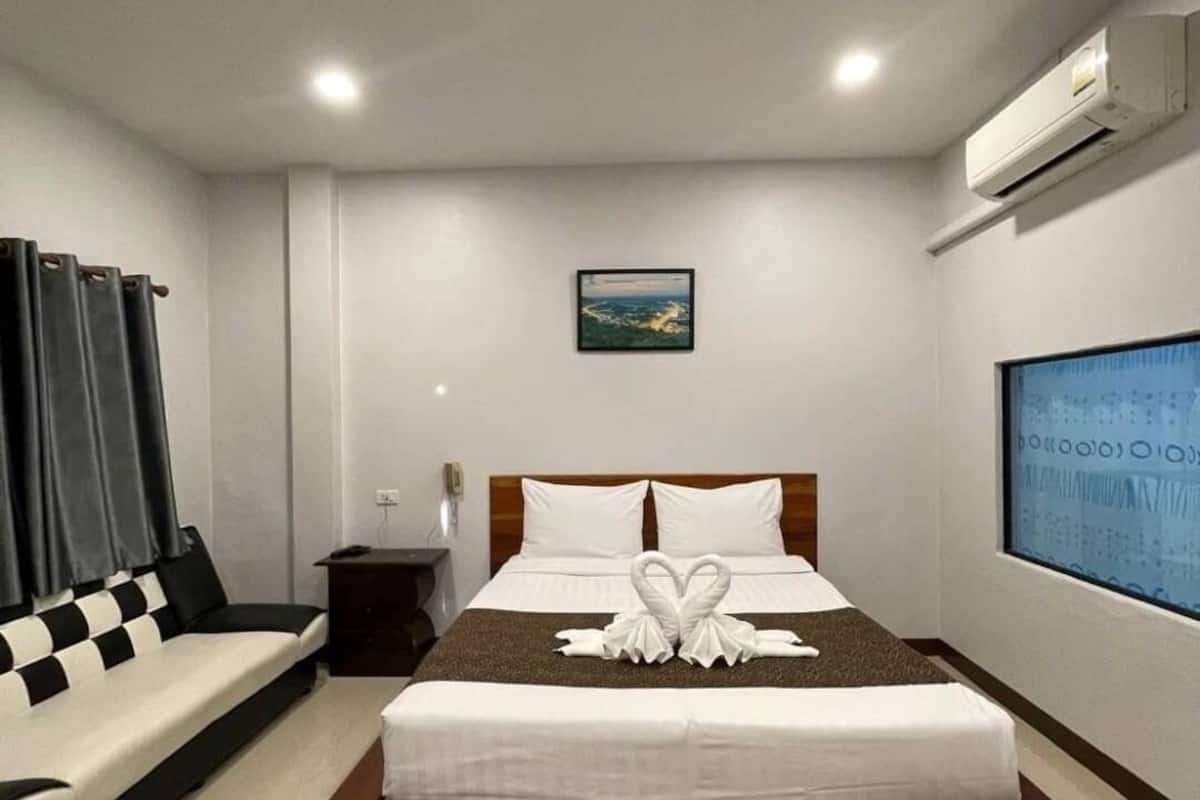A modern hotel room with a large bed, a small bedside table, a wall-mounted air conditioner, and a large window.