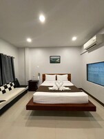 Una habitación de hotel moderna con una cama grande, una mesita de noche pequeña, un aire acondicionado de pared y un ventanal amplio.