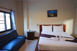 Una habitación de hotel con cama, sofá, mesita de noche y televisor montado en la pared.