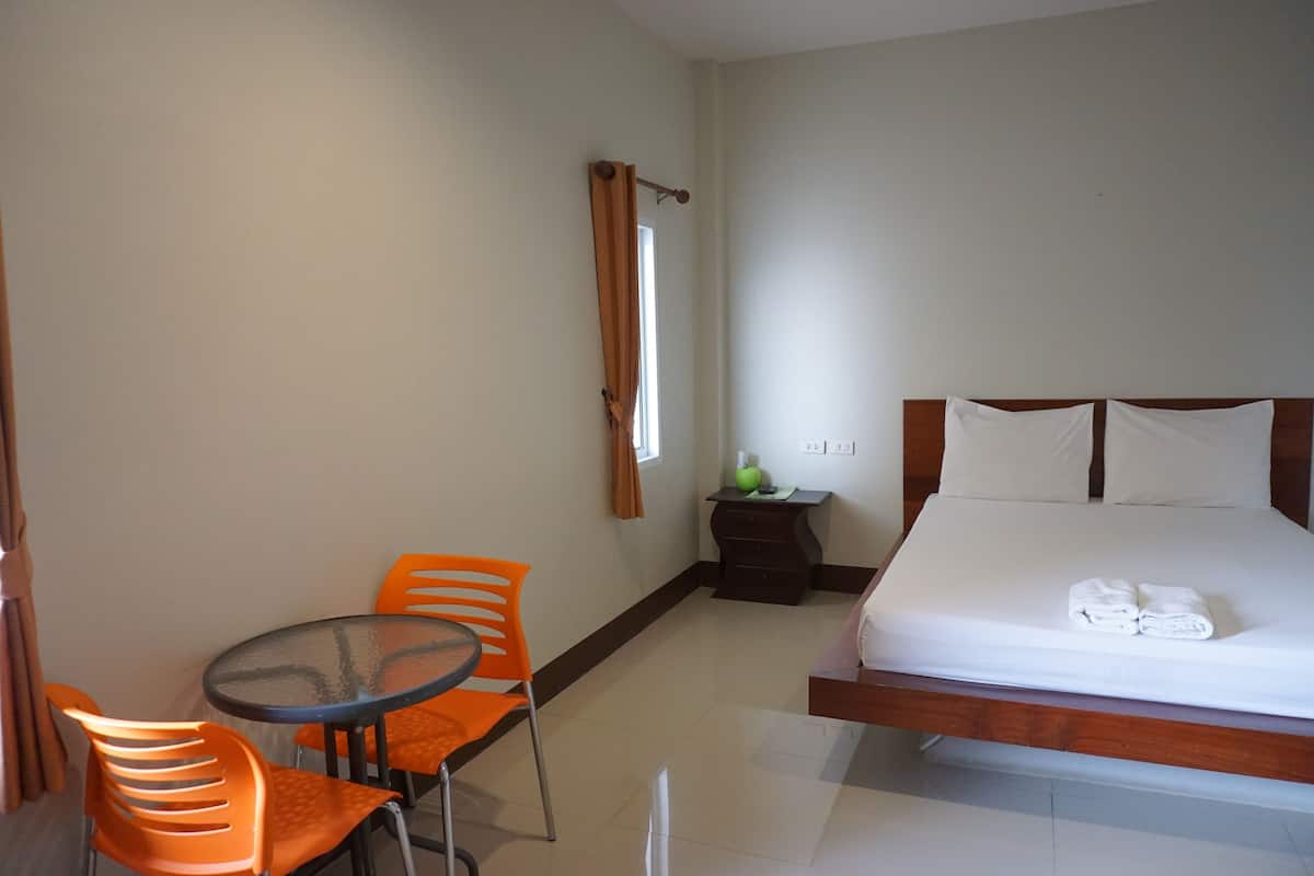 A hotel room with a bed, a small table with two chairs, a nightstand, and a window with curtains.