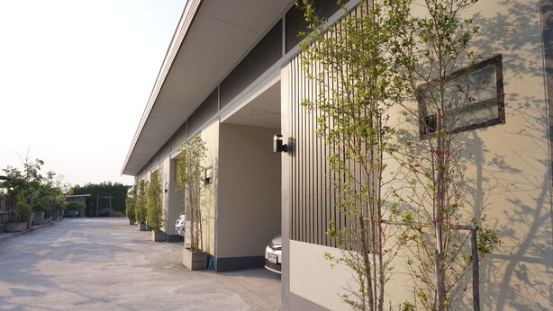 Un edificio moderno con un paseo techado, plantas en macetas y un coche estacionado.