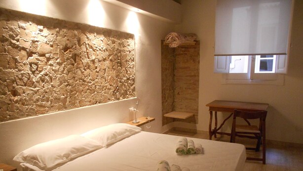 Ein Schlafzimmer mit einer Steinwand, einem Holzkopfstück, einem Nachttisch aus Holz, einem Holztisch und einem Fenster mit Jalousien.