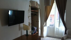 Ein Zimmer mit Fernseher, Schreibtisch, Stuhl und Blick durch eine Tür nach draußen.