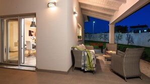 Eine Terrasse im Freien mit Korbmöbeln, einem Tisch mit Getränken und Blick auf den Garten.