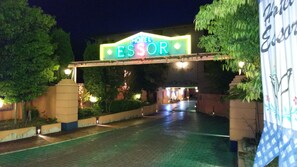 A hotel entrance with a neon sign, paved walkway, and greenery. - HOTEL ESSOR - Adult Only (Nara)