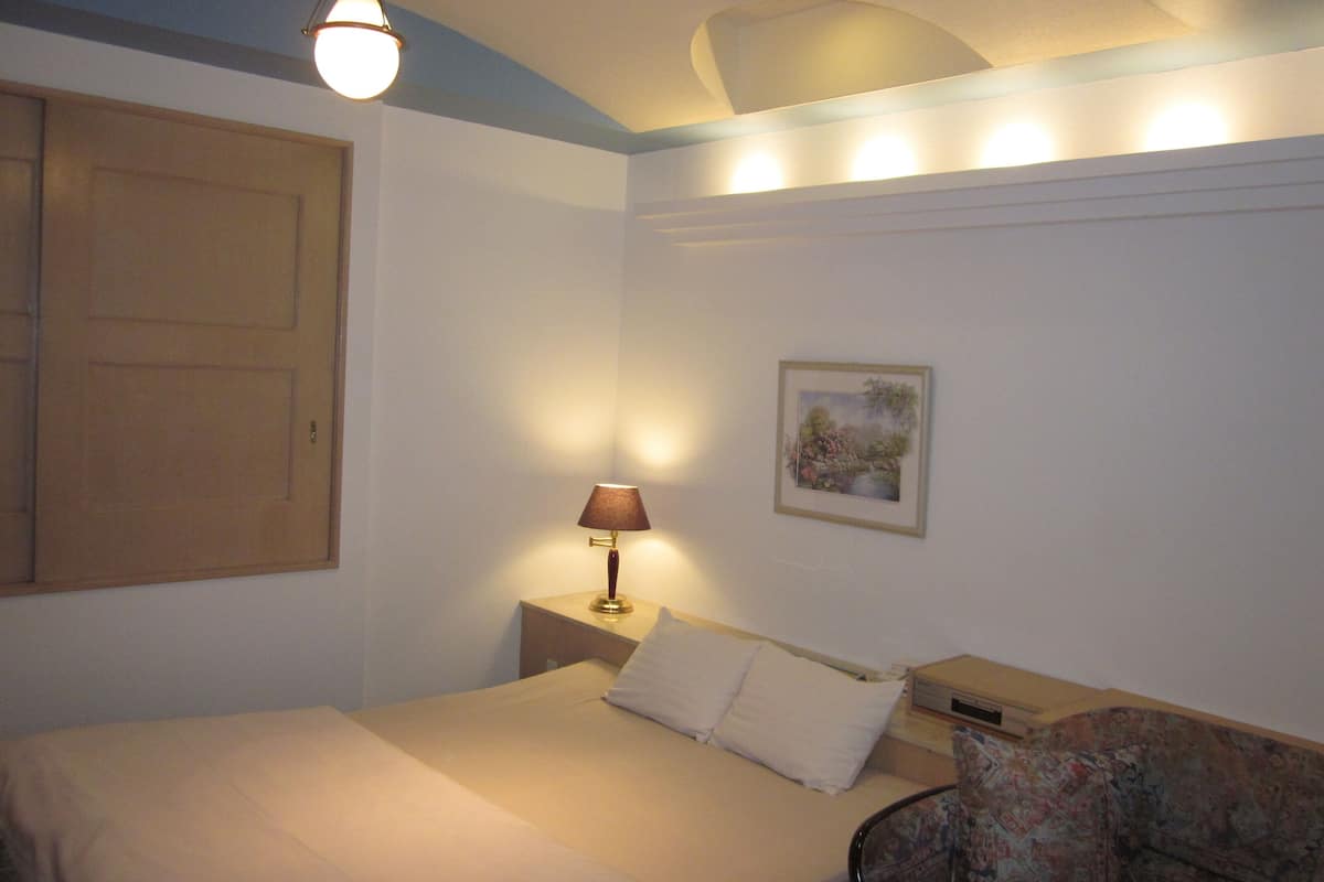 A bedroom with a bed, a nightstand, a lamp, a framed picture, and a door.