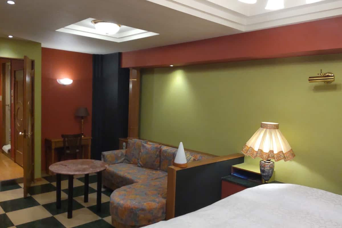 A hotel room with a bed, a sofa, a small table, a lamp, and a checkered floor.