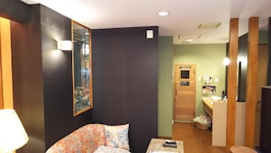 A hotel room with a large mirror, a bed with floral bedding, a small table with a remote control, and a wooden door leading to a bathroom with a sauna sign. - HOTEL ESSOR - Adult Only (Nara)