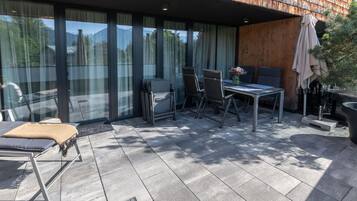 Een modern terras buiten met een eettafel, stoelen en een zithoek.